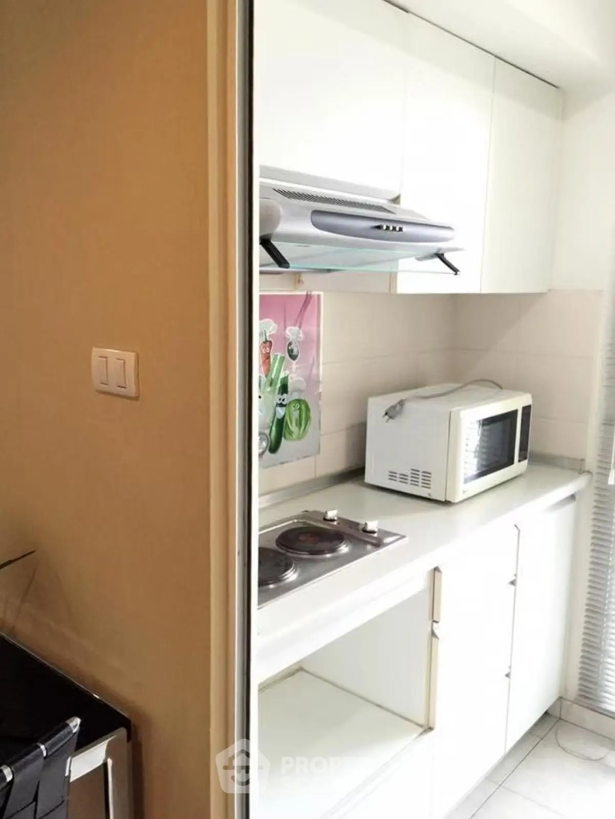 Compact kitchen with white cabinets, microwave, and electric stove in modern apartment.