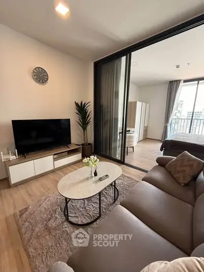 Modern living room with cozy seating and TV, adjacent to a stylish bedroom with balcony view.