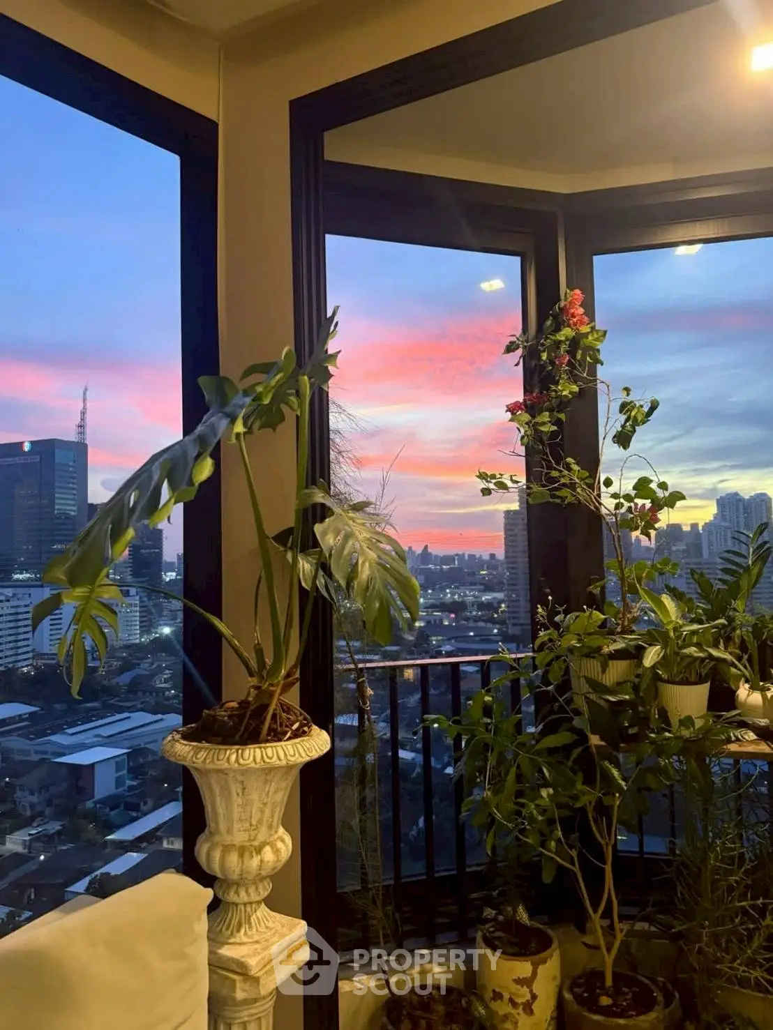 Stunning corner unit with panoramic city view and lush indoor plants at sunset.