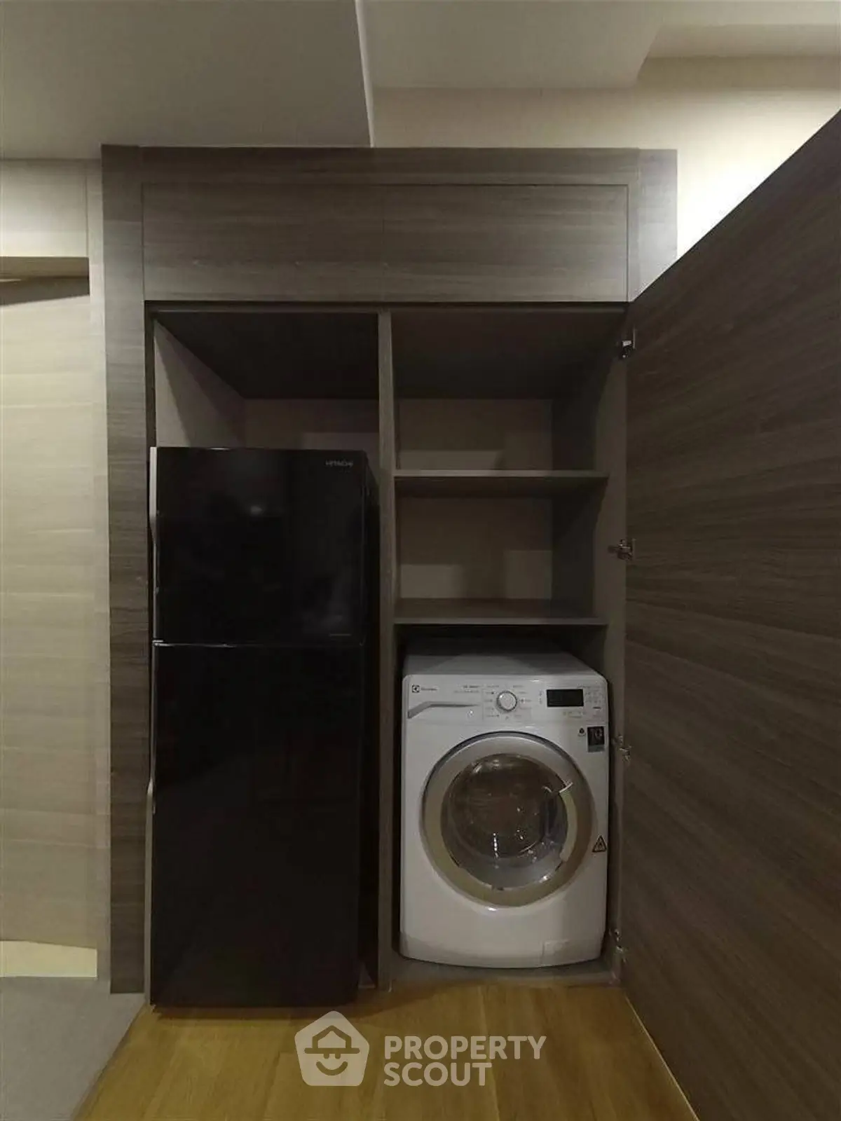 Compact laundry and storage area with washing machine and fridge in modern apartment.