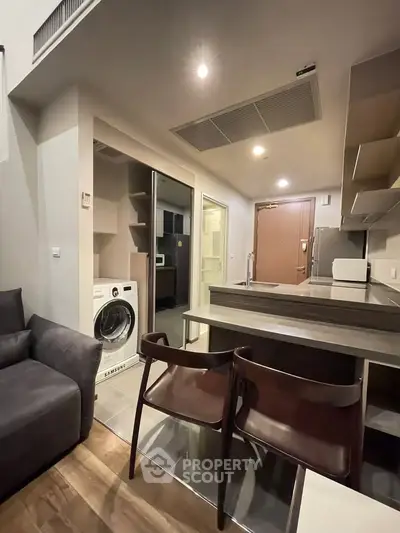Modern apartment interior with open kitchen and washing machine, featuring sleek design and cozy seating area.