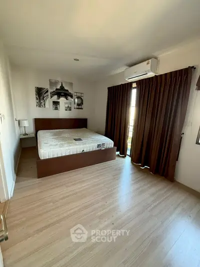 Spacious bedroom with wooden flooring and large window for natural light