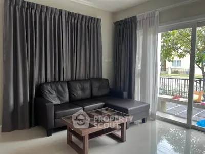 Modern living room with sleek black sofa and large windows overlooking a garden.
