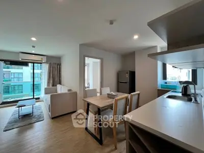 Modern open-plan living room with kitchen in a bright apartment, featuring stylish furniture and large windows.