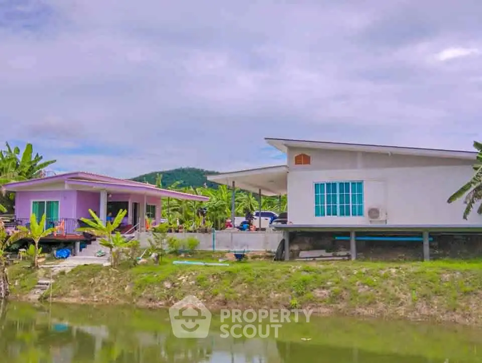 Charming rural homes by a serene pond with lush greenery and mountain views.