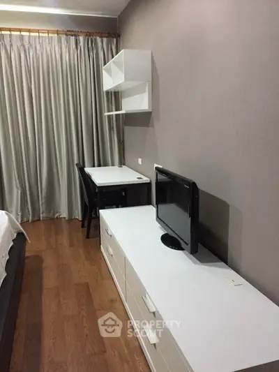 Modern bedroom with sleek furniture and wooden flooring, featuring a compact workspace and stylish decor.