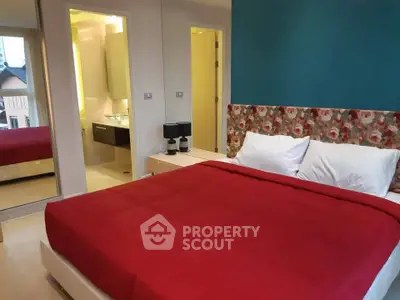 Modern bedroom with vibrant red bedding and stylish decor, featuring an ensuite bathroom and mirrored wardrobe.