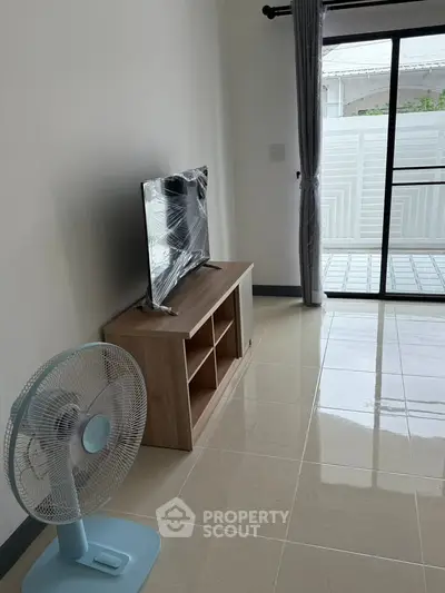 Modern living room with TV stand and fan, featuring large sliding glass door to balcony.