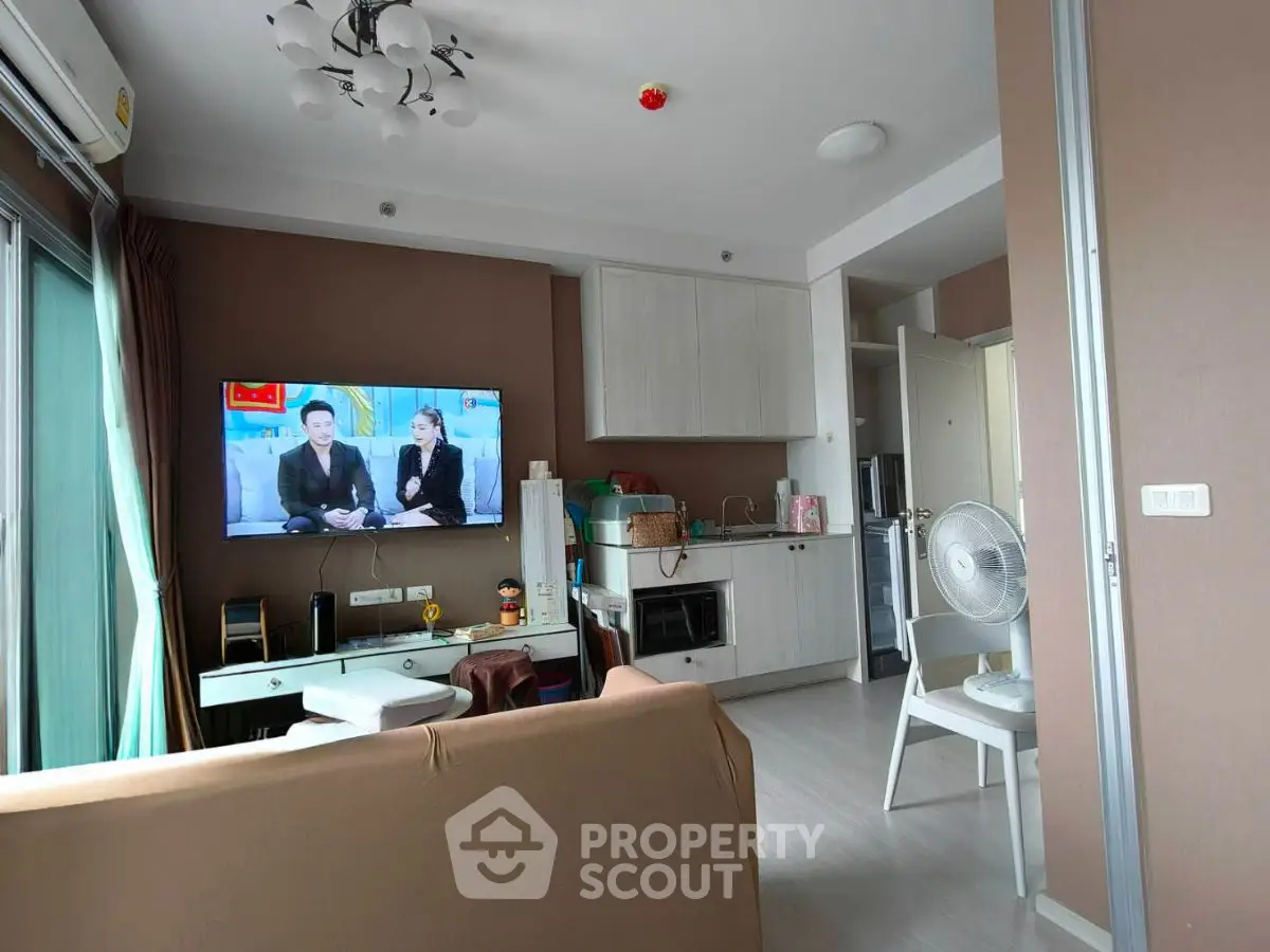 Modern living room with TV, sofa, and compact kitchen in open layout apartment.