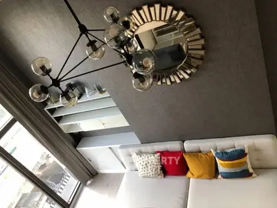 Stylish modern living room with unique chandelier and colorful cushions on a white sofa.