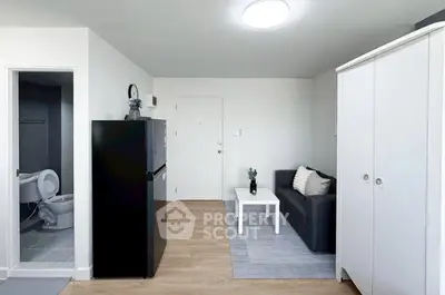 Modern studio apartment with sleek black fridge, cozy sofa, and compact bathroom.