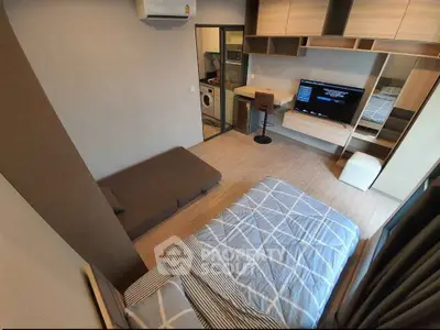 Modern bedroom with stylish decor, featuring a cozy bed, wall-mounted TV, and compact laundry area.