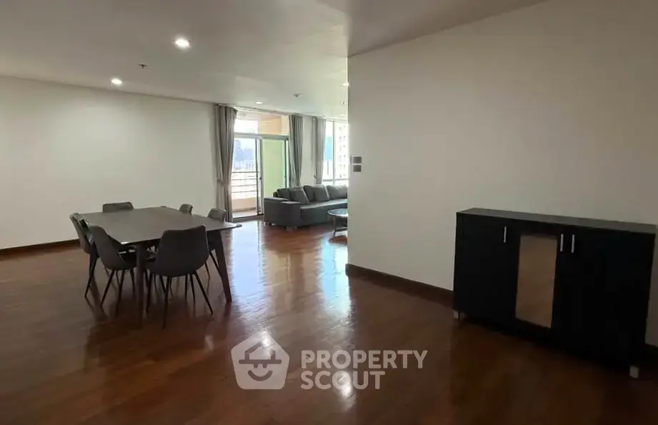 Spacious modern living room with dining area and balcony access, featuring sleek furniture and wooden flooring.