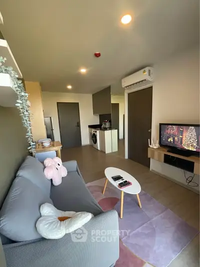 Modern living room with cozy sofa, TV, and compact kitchen in open layout apartment.