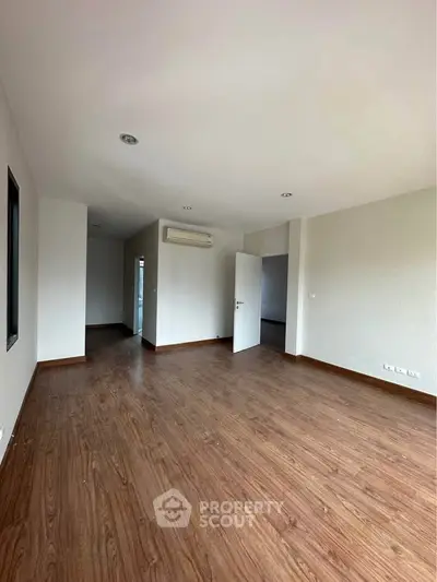 Spacious empty room with wooden flooring and air conditioning, ideal for customization.