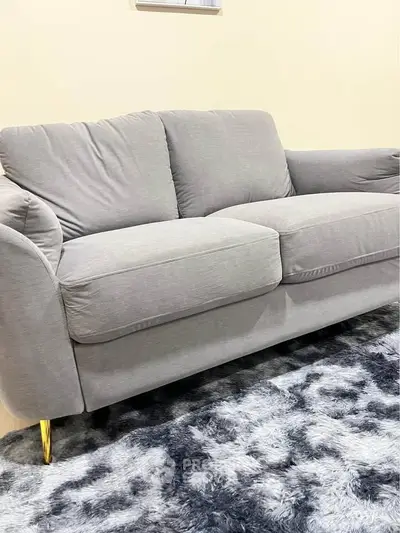 Stylish gray sofa with plush cushions on a modern patterned rug, perfect for a cozy living room.