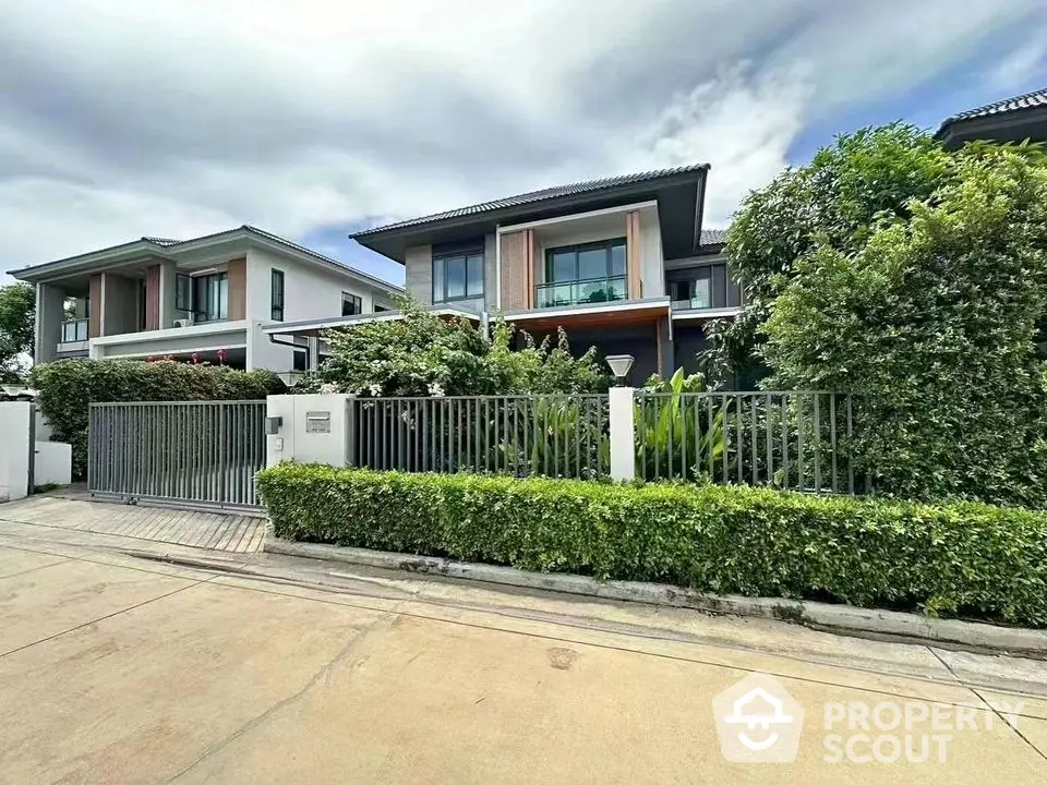 Modern two-story house with lush greenery and sleek metal fence in a suburban neighborhood.