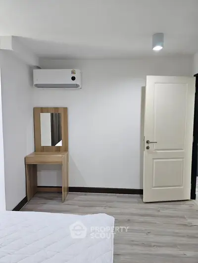Minimalist bedroom with air conditioning and wooden vanity, perfect for modern living.
