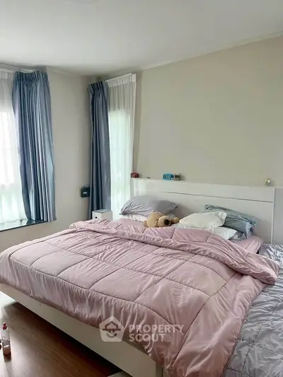 Cozy bedroom with soft pink bedding and natural light from large windows.