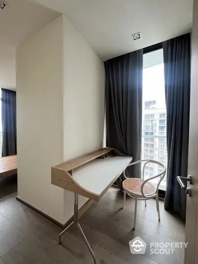 Modern study nook with sleek desk and chair, large window with city view, elegant curtains, and wooden flooring.