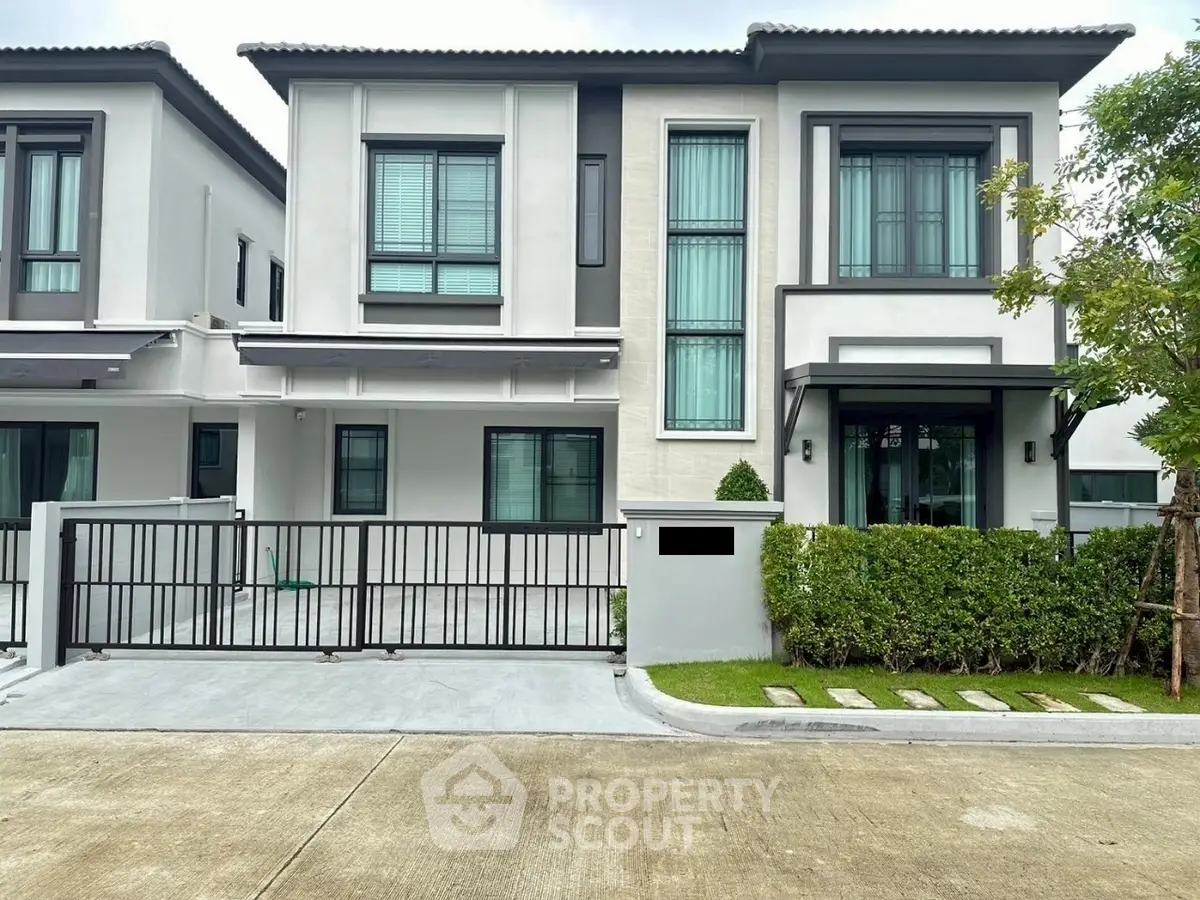 Modern two-story house with sleek design and lush greenery in a suburban neighborhood.