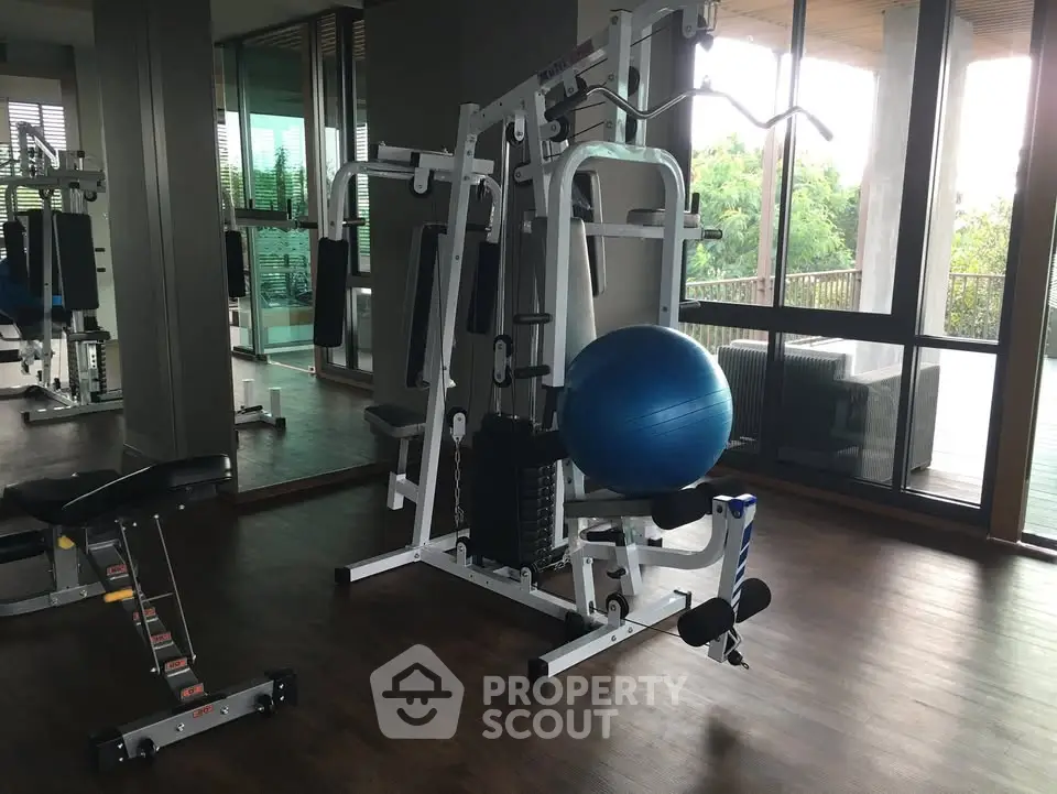 Modern gym with exercise equipment and large windows overlooking greenery.