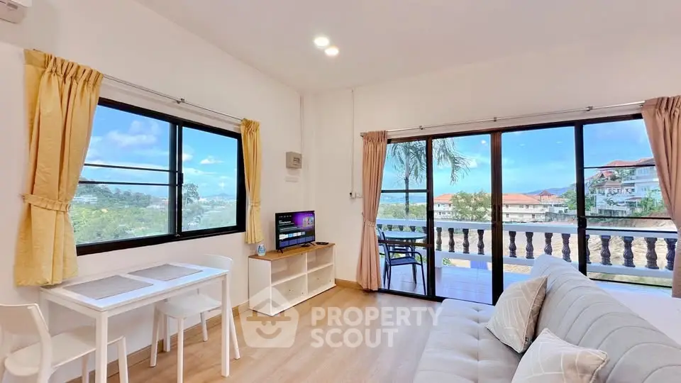 Bright living room with balcony and scenic view, featuring modern furniture and large windows.