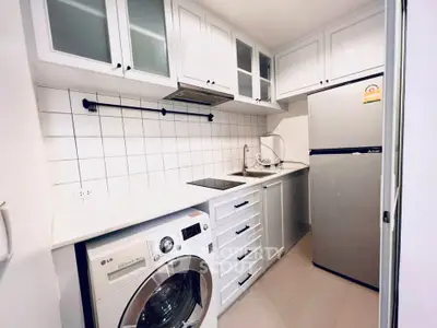 Modern compact kitchen with white cabinetry, washing machine, and stainless steel fridge.