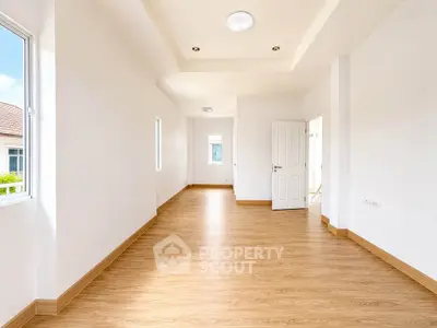 Spacious empty room with wooden flooring and bright natural light, ideal for customization.