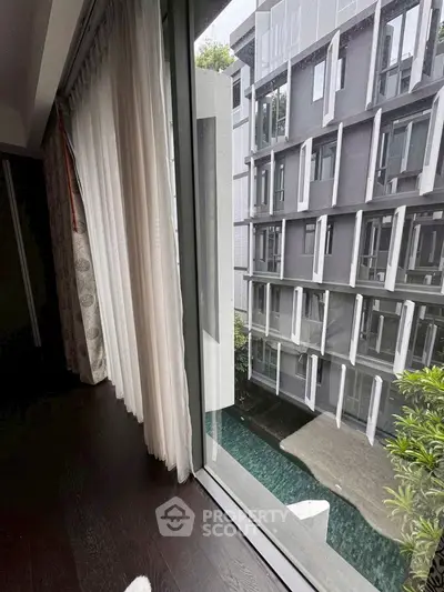Modern apartment view with floor-to-ceiling windows overlooking a stylish building and pool area.
