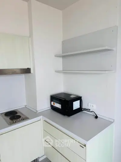Modern kitchen corner with sleek cabinets and built-in stovetop, featuring a microwave and open shelving.
