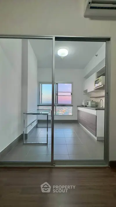 Modern kitchen with glass sliding doors and city view, featuring sleek cabinetry and tiled flooring.