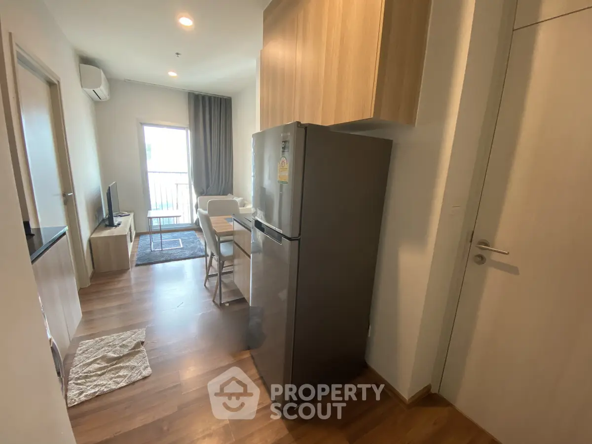 Modern apartment interior with open kitchen and cozy living area, featuring wooden flooring and natural light.