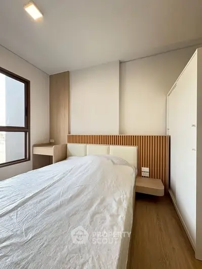 Modern bedroom with minimalist design and natural light, featuring wooden accents and a large window.