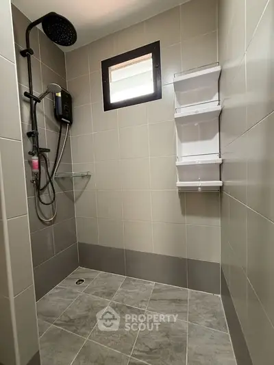 Modern bathroom with sleek shower and tiled walls, featuring a window for natural light.
