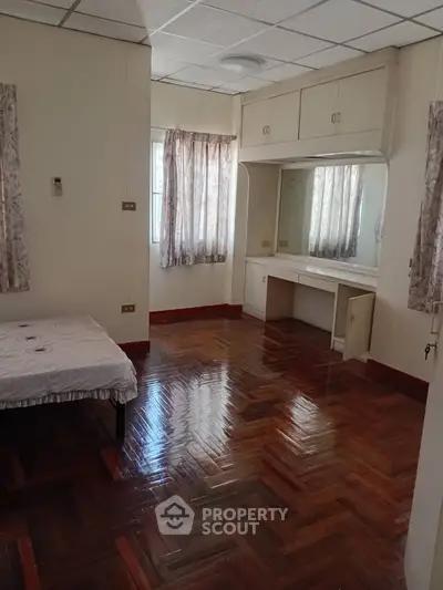 Spacious bedroom with polished wooden floors and built-in vanity, featuring natural light from large windows.
