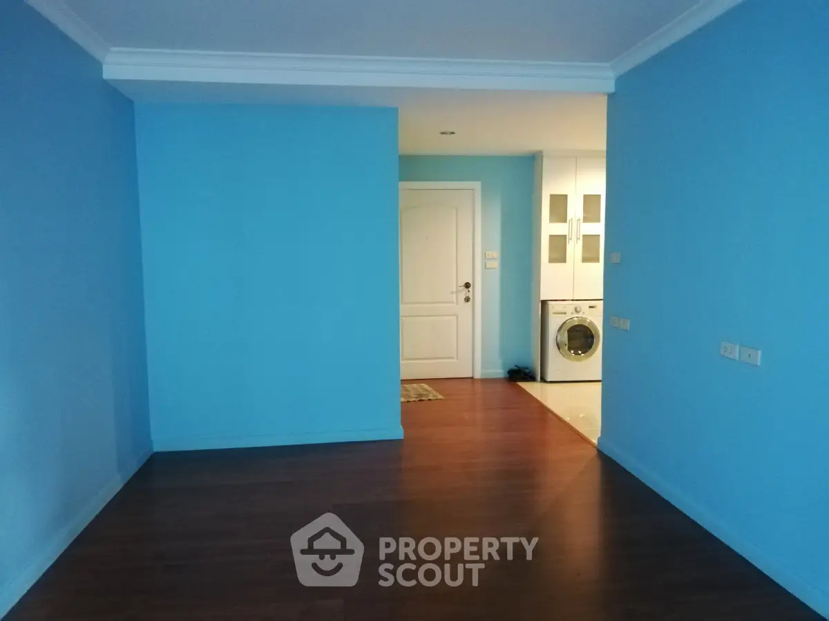 Spacious blue-walled room with wooden flooring and a washing machine near the entrance.