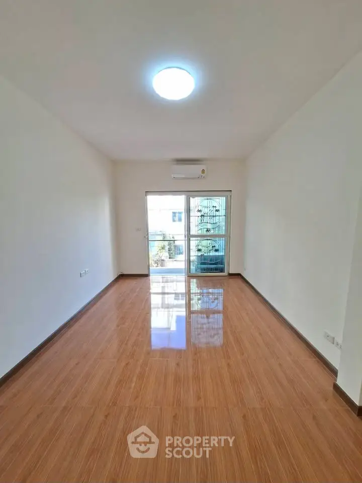 Spacious empty room with glossy wooden flooring and large window.