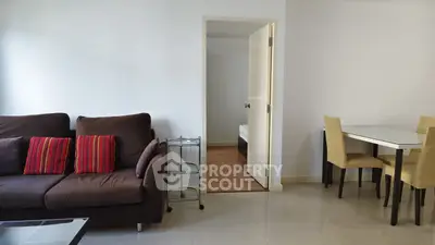 Modern living room with brown sofa, dining table, and open door to bedroom.