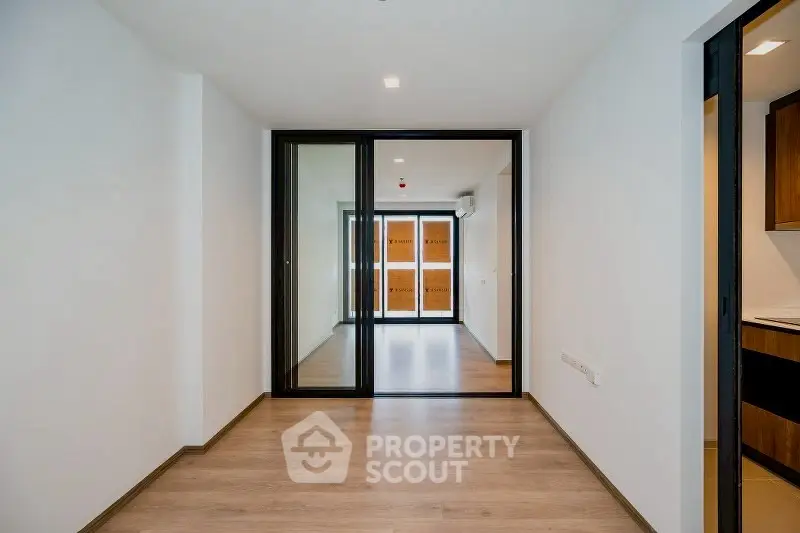 Modern apartment interior with wooden flooring and glass sliding doors leading to a bright living area.
