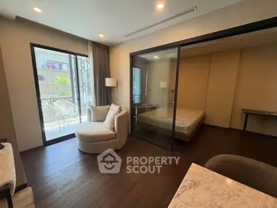 Modern living room with cozy seating and view into a bedroom through glass doors.