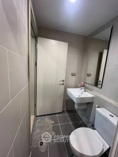 Modern bathroom with sleek design and neutral tiles, featuring a compact sink and toilet.
