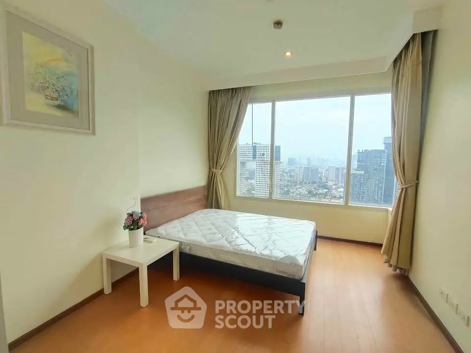 Bright bedroom with large window offering stunning city view, featuring minimalist decor and wooden flooring.