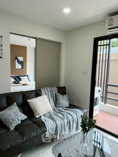 Modern living room with balcony and bedroom view, featuring stylish decor and natural light.