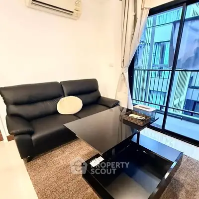 Modern living room with sleek black sofa and glass coffee table, featuring large window with city view.