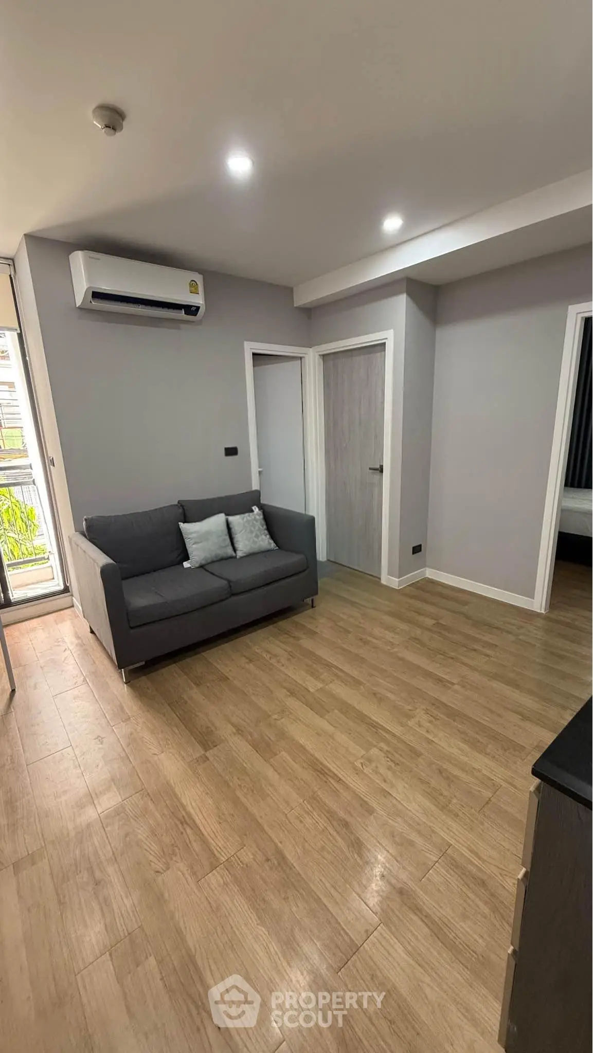 Modern living room with sleek design and wooden flooring, featuring a cozy gray sofa and air conditioning.