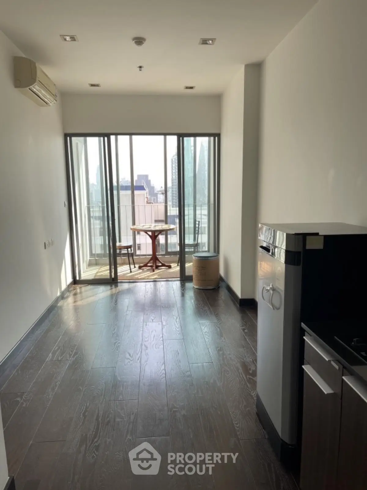 Modern apartment with balcony and city view, featuring sleek flooring and compact kitchen area.