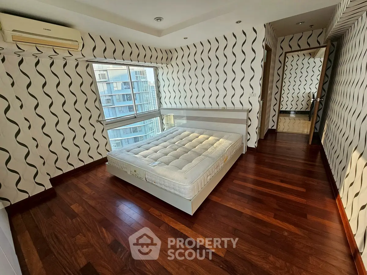 Spacious bedroom with modern design and wooden flooring in high-rise apartment.