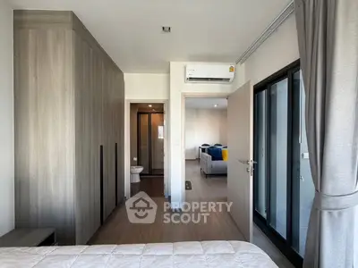 Modern bedroom with ensuite bathroom and large window, featuring sleek wood finishes and air conditioning.