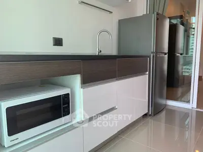 Modern kitchen with sleek cabinetry, microwave, and stainless steel fridge in a stylish apartment.
